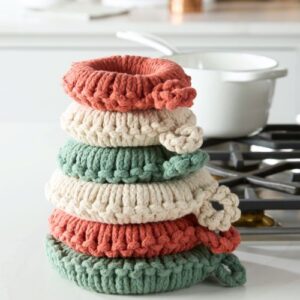 Stack of Cream/Clay/Green crocheted trivet sets on kitchen counter with enamel cookware