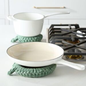 Green crocheted trivet set on kitchen counter with enamel cookware