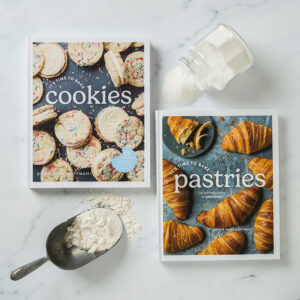 It's Time to Bake Cookies and It's Time to Bake Pastries Books on white marble background surrounded by backing ingredients