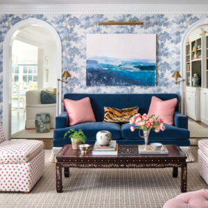 Living room with navy velvet couch, blue and white wallpaper, and pink pillows