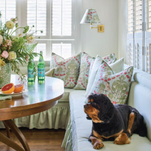Breakfast nook with green and pink pillows, brown table, and cavalier dog