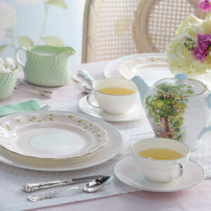 Table setting for tea with white teapot and pink tablecloth